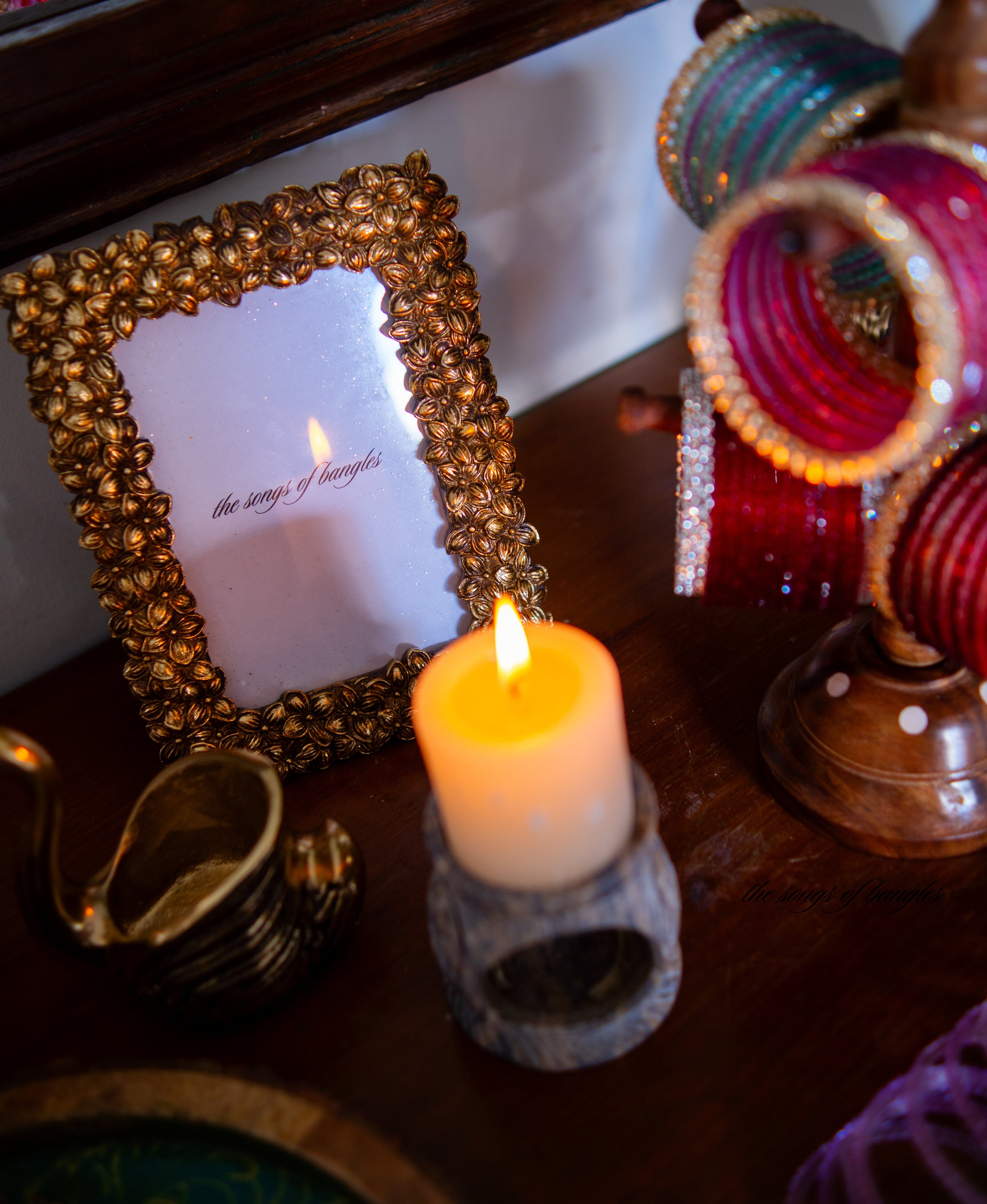 Decorative setup with a lit candle, gold-framed photo, and colorful bracelets on a wooden surface.